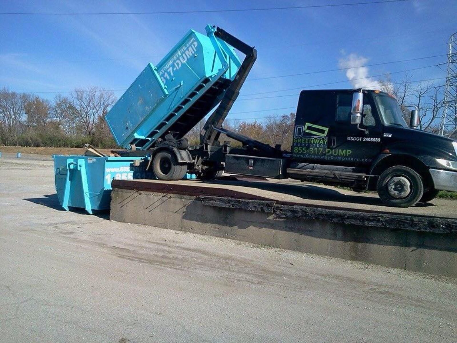Greenway truck dumping a dumpster into another dumpster.