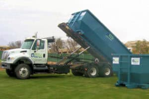 A Greenway truck unloading a dumpster at a job site.