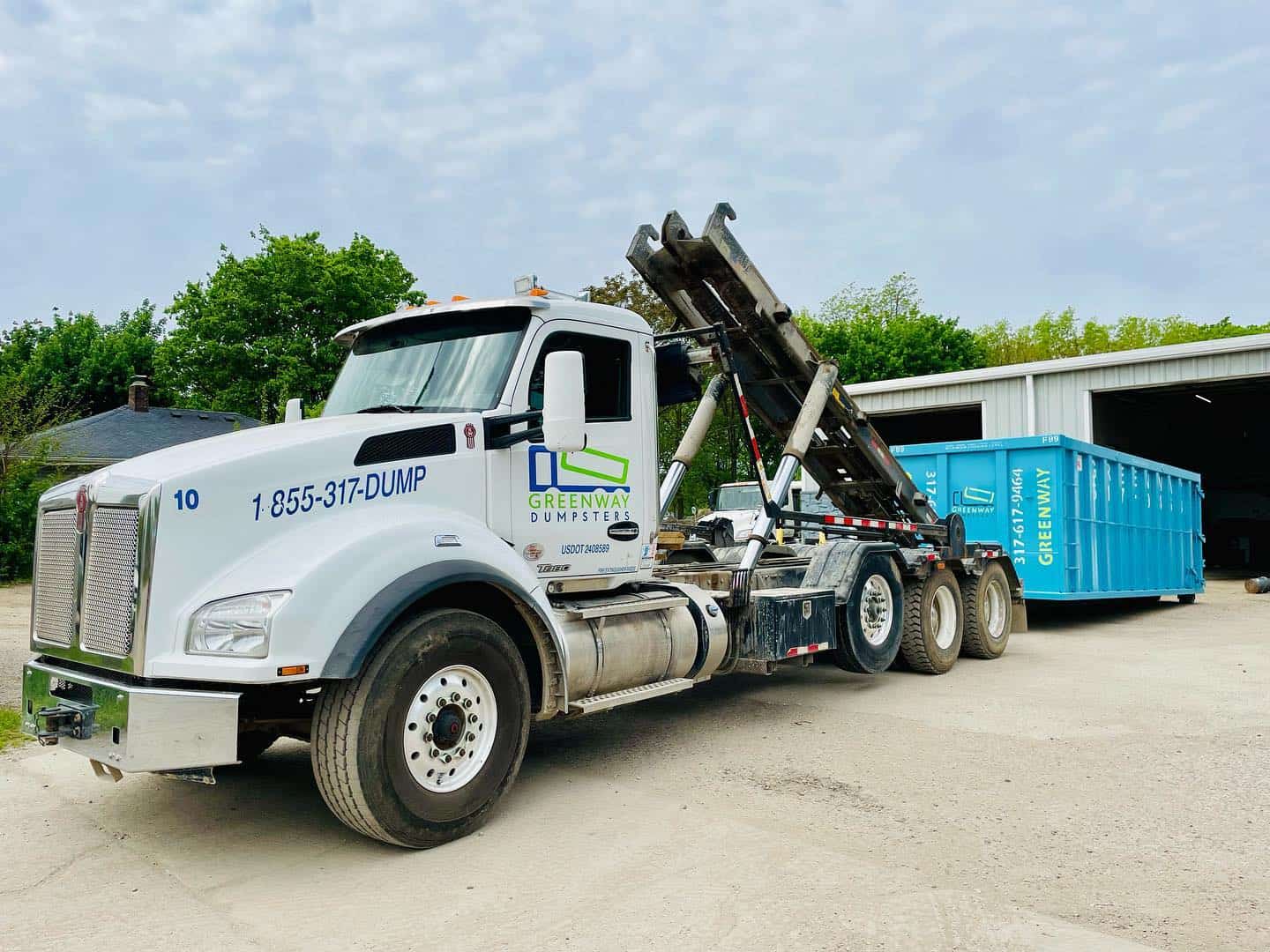 A Greenway truck unloading a dumpster at a job site.